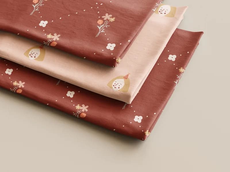 Folded fabric swatches printed with the Bottega Lily character pattern in terracotta and blush